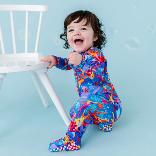 Child in colorful outfit sitting on floor with blue background