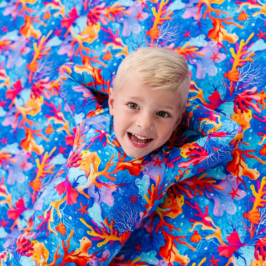 Child under a colorful coral-patterned blanket
