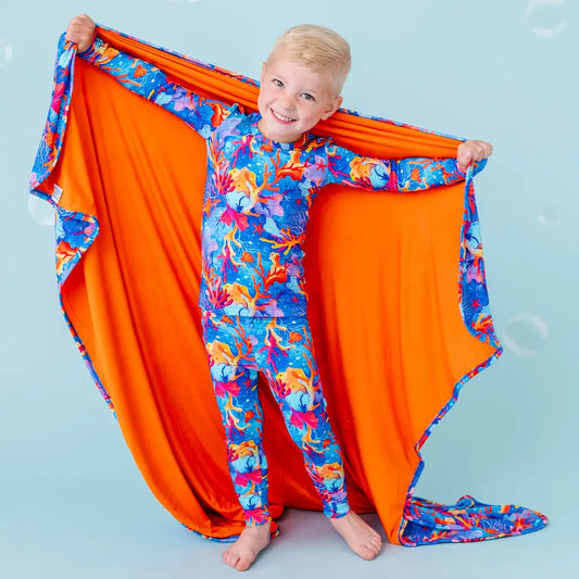 A child holding up a blanket with a vibrant coral and sea creature pattern in orange, blue, and purple colors.