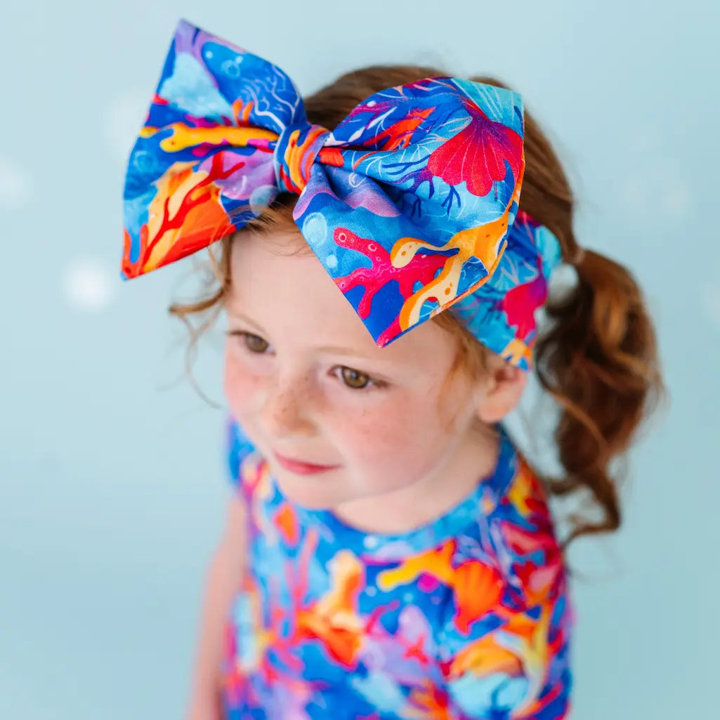 A child with a colorful bow headband with a reef and coral pattern.