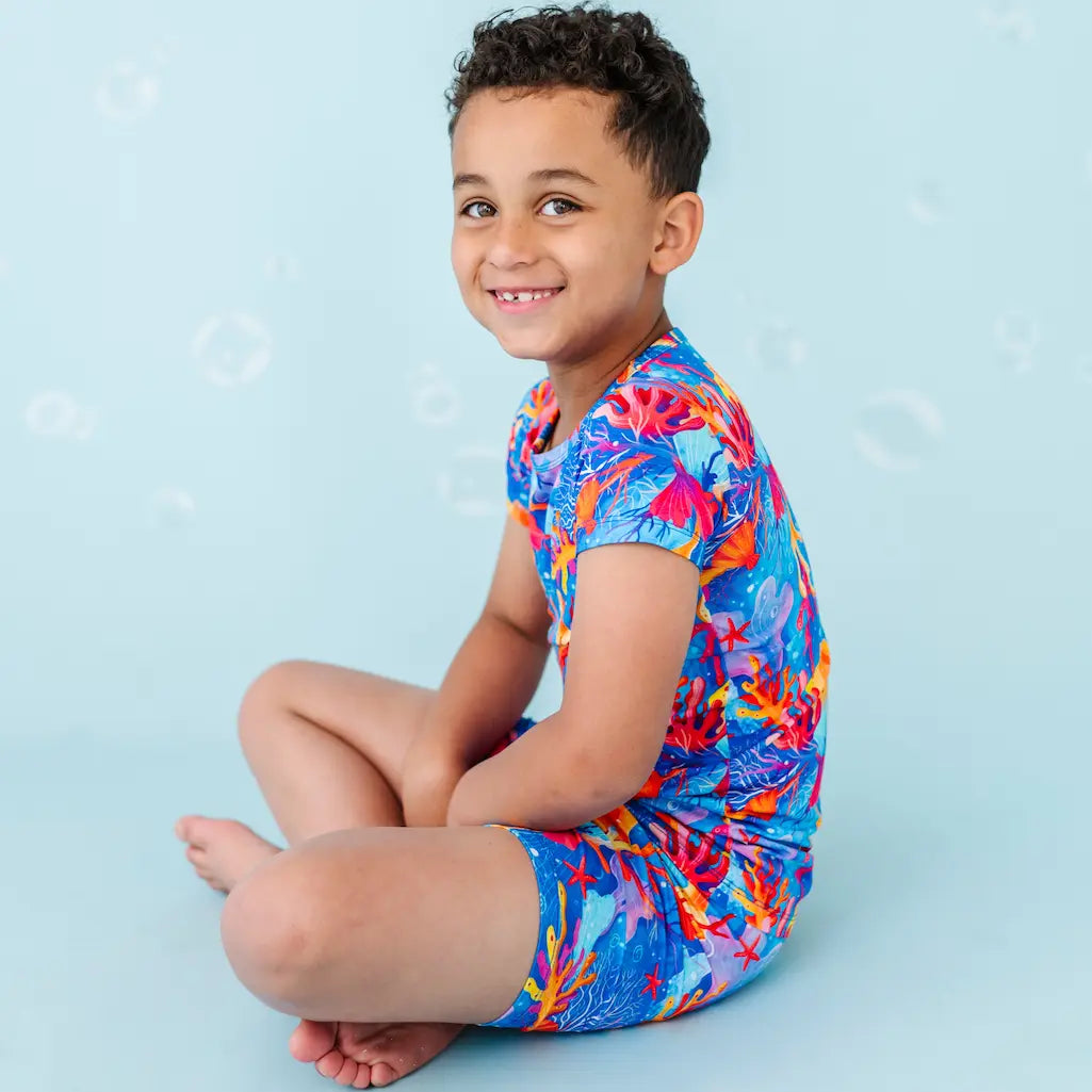 Child wearing a colorful coral reef-themed swimsuit sitting on a blue background.