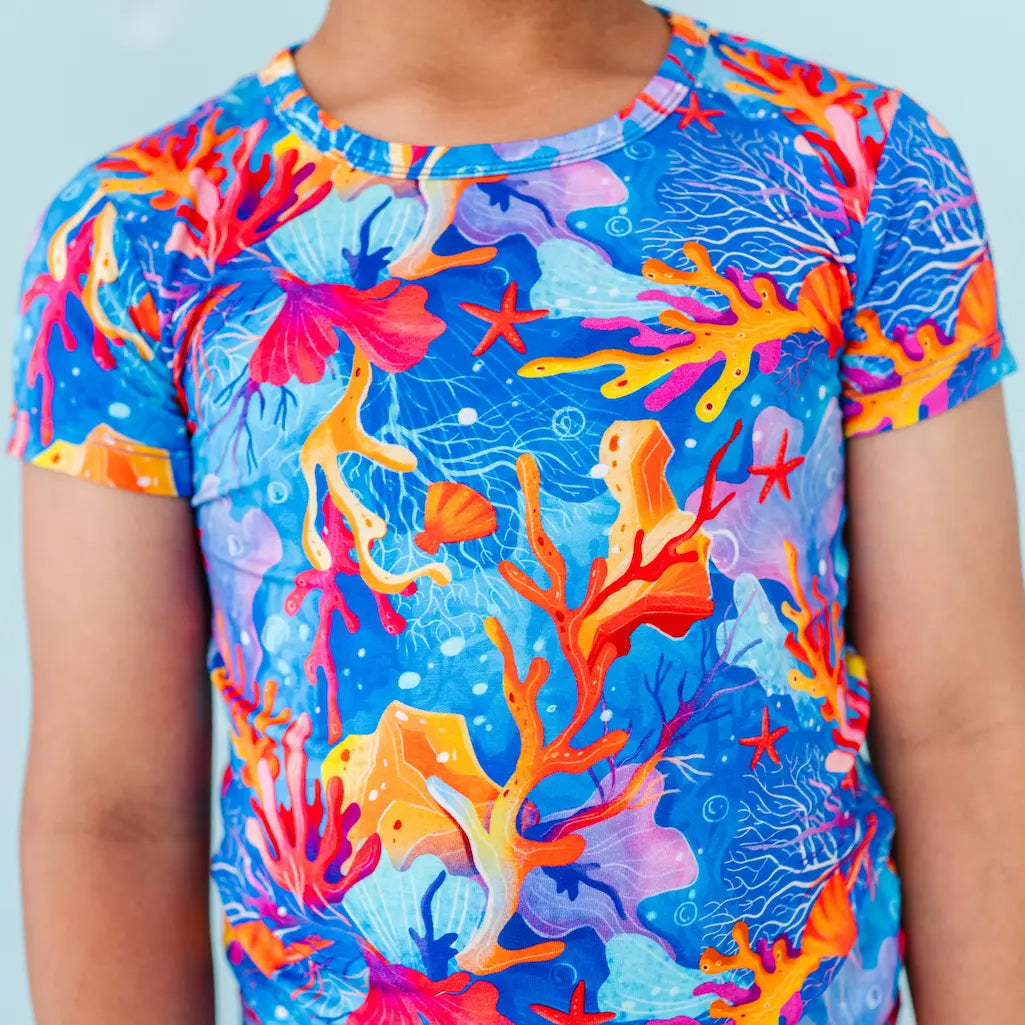 Child wearing a colorful coral-themed t-shirt against a light blue background