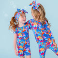 Two children wearing colorful coral-themed swimsuits against a light blue background.