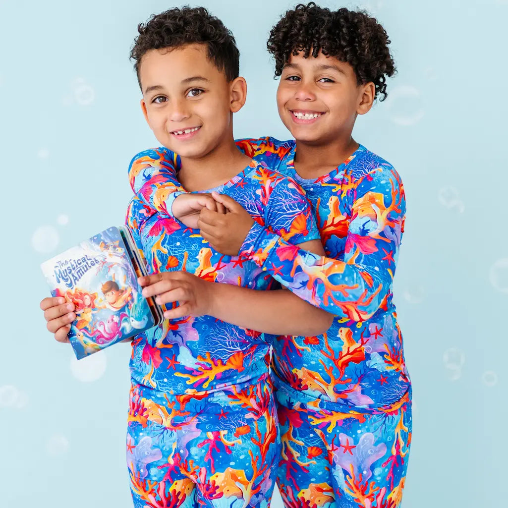 Two children in matching colorful outfits holding a book against a light blue background.