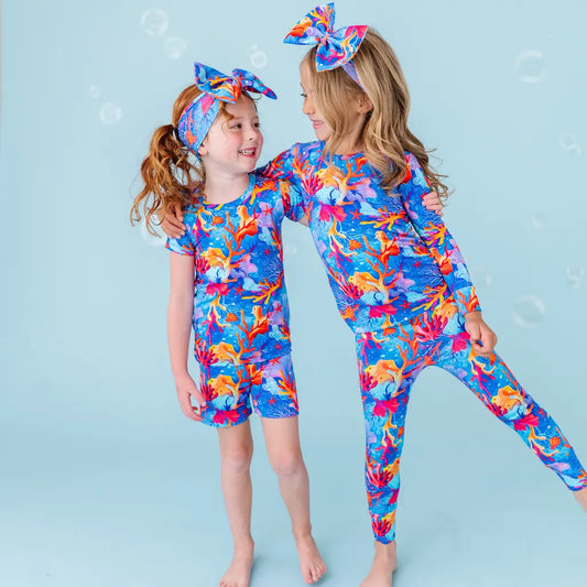 Two children in colorful outfits and headbands standing close together on a light blue background.