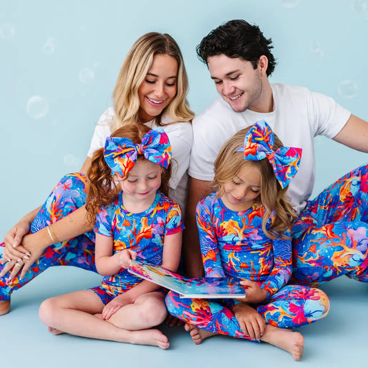 Family of four wearing matching colorful outfits, sitting on a blue background.