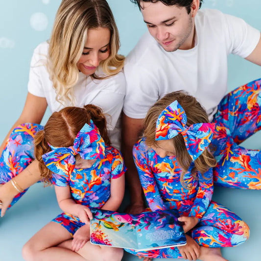 Family wearing matching colorful outfits reading a book against a light blue background.