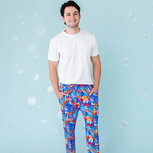 A man wearing white t-shirt and multicolored pajama pants with a tropical coral pattern.