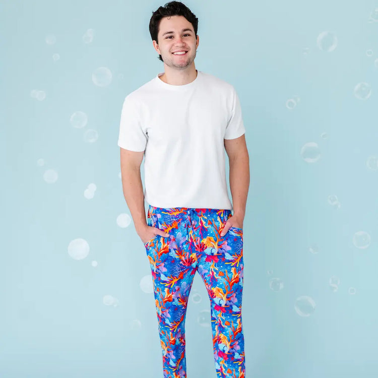 A man wearing white t-shirt and multicolored pajama pants with a tropical coral pattern.