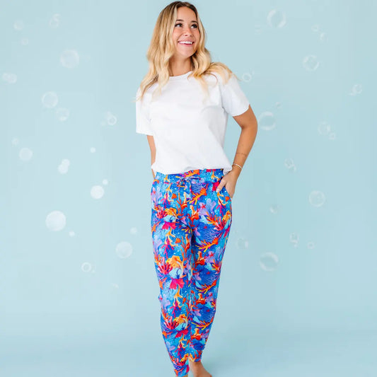 A woman standing and smiling, wearing white shirt and multicolored pajama pants with a coral reef pattern.