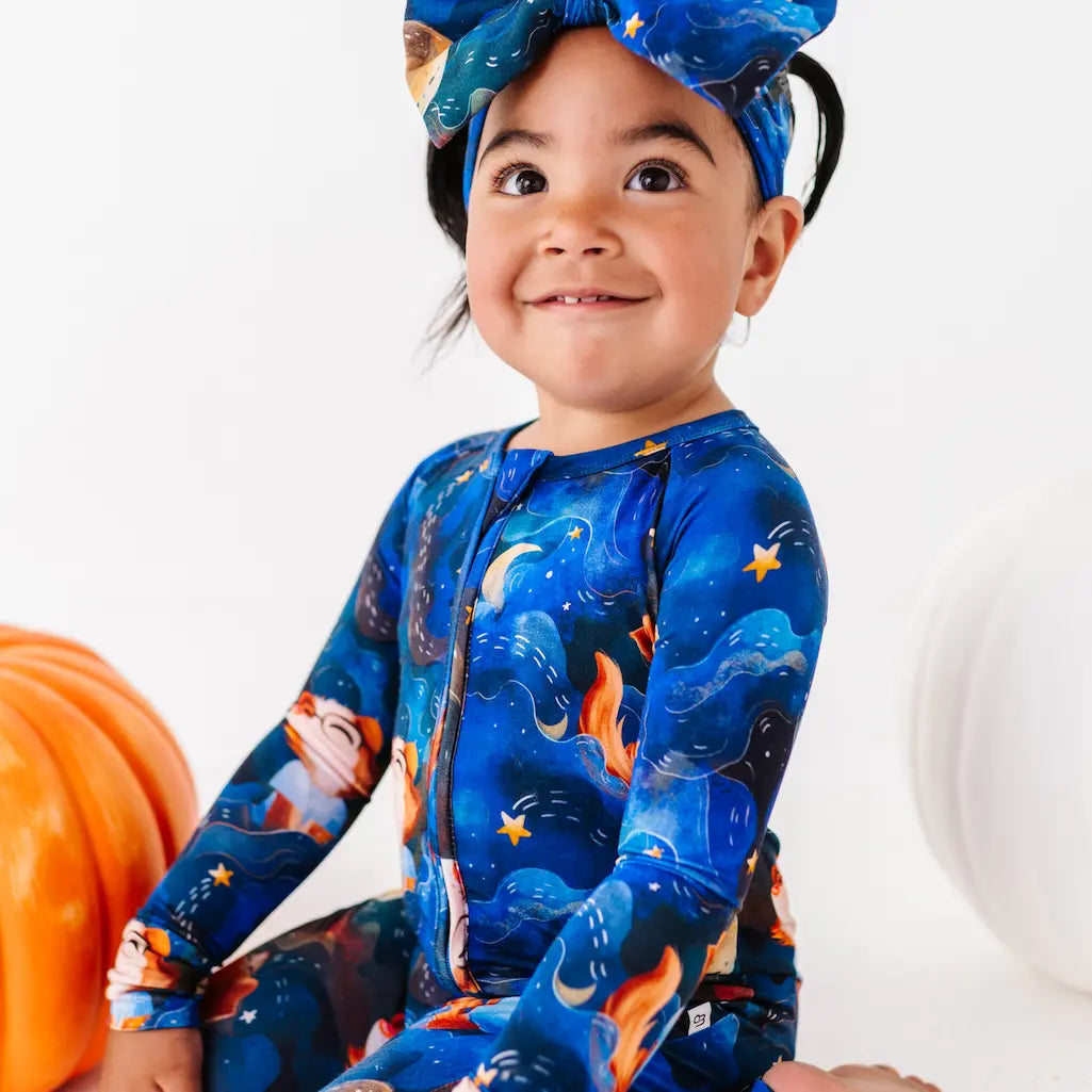 Child wearing a blue space-themed onesie with stars and planets, sitting next to a pumpkin.