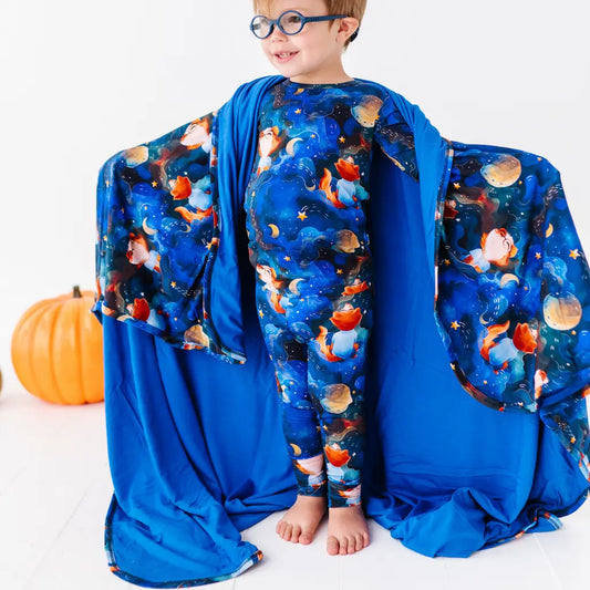 Child wearing a blue space-themed onesie with a matching blanket, standing next to a pumpkin on a white background.