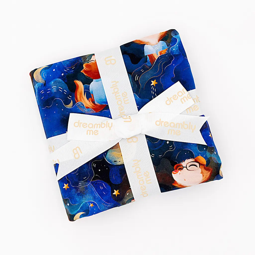 Set of four Dreambly Me product packages with blue and orange artistic designs tied together with a cream 'dreambly me' ribbon on a white background