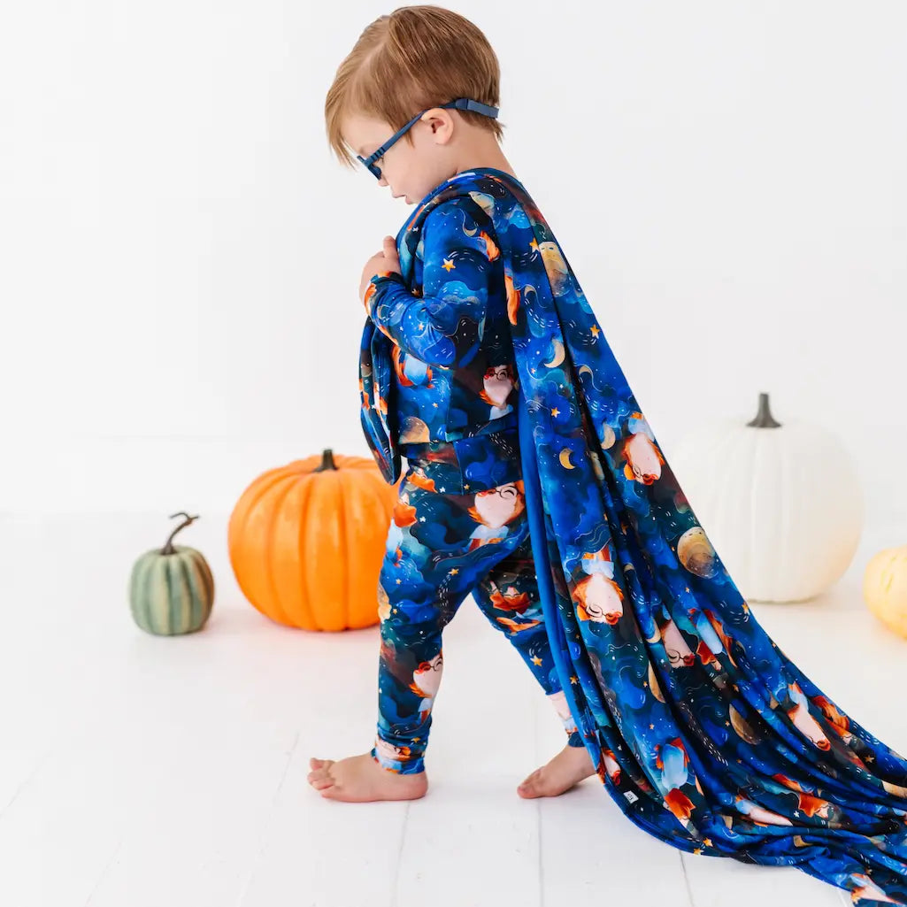Child wearing a blue cape with animal prints, standing in front of pumpkins on a white background