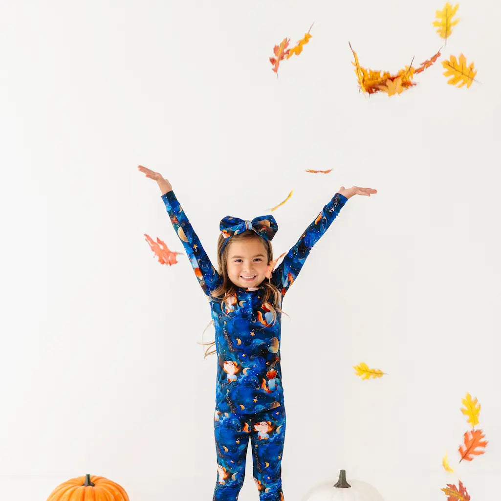 Child wearing a blue onesie with animal prints, surrounded by autumn leaves and pumpkins on a white background.