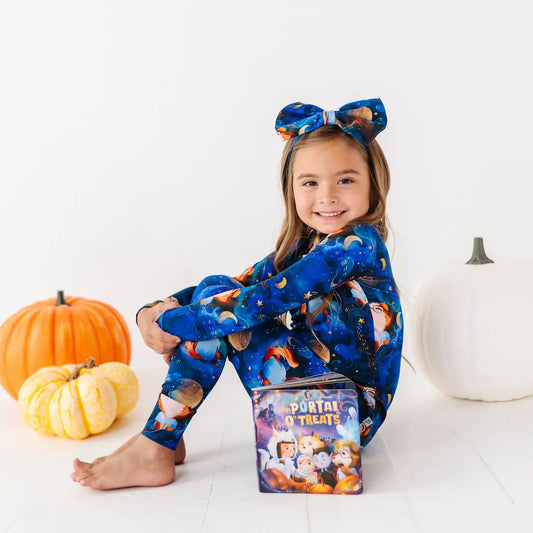 Child wearing a blue Halloween-themed onesie with pumpkins and a box of treats on a white background.