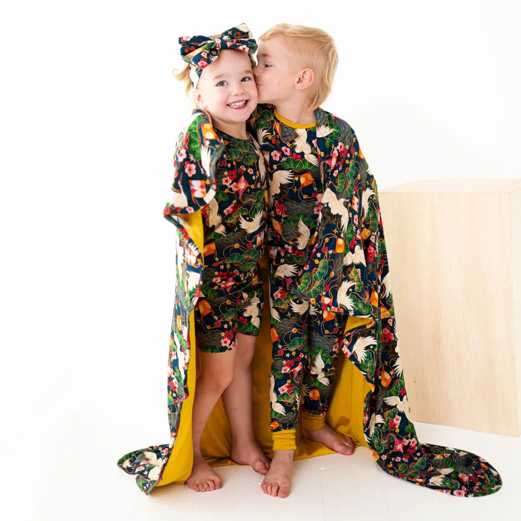 Two children wearing colorful animal-patterned pajamas with a matching blanket.