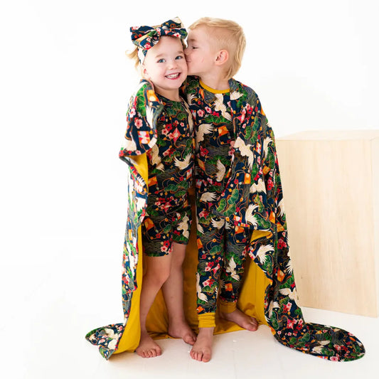 Two children wearing colorful animal-patterned pajamas with a matching blanket.