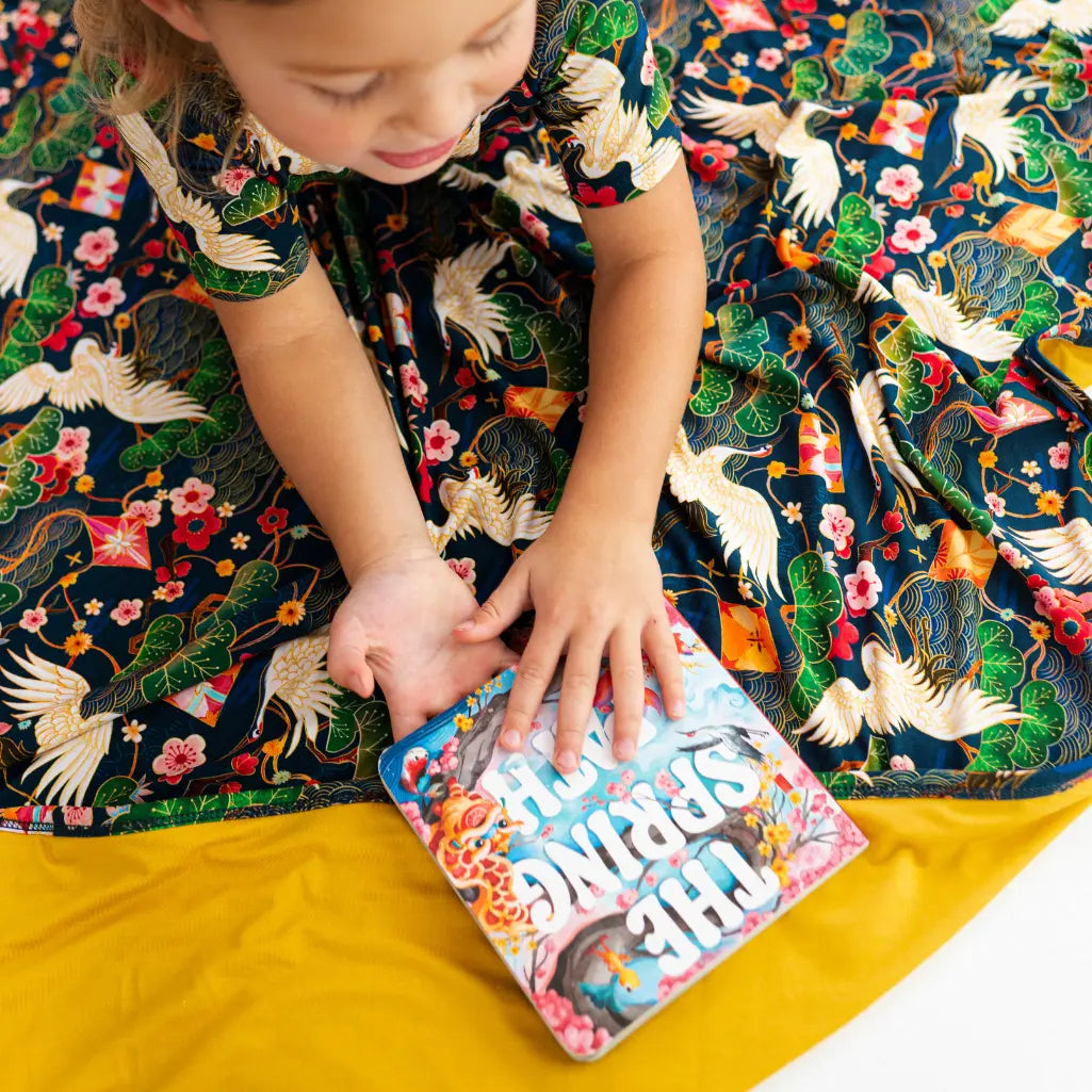 Child interacting with a book titled 'Riding the Waves' on a colorful patterned blanket.