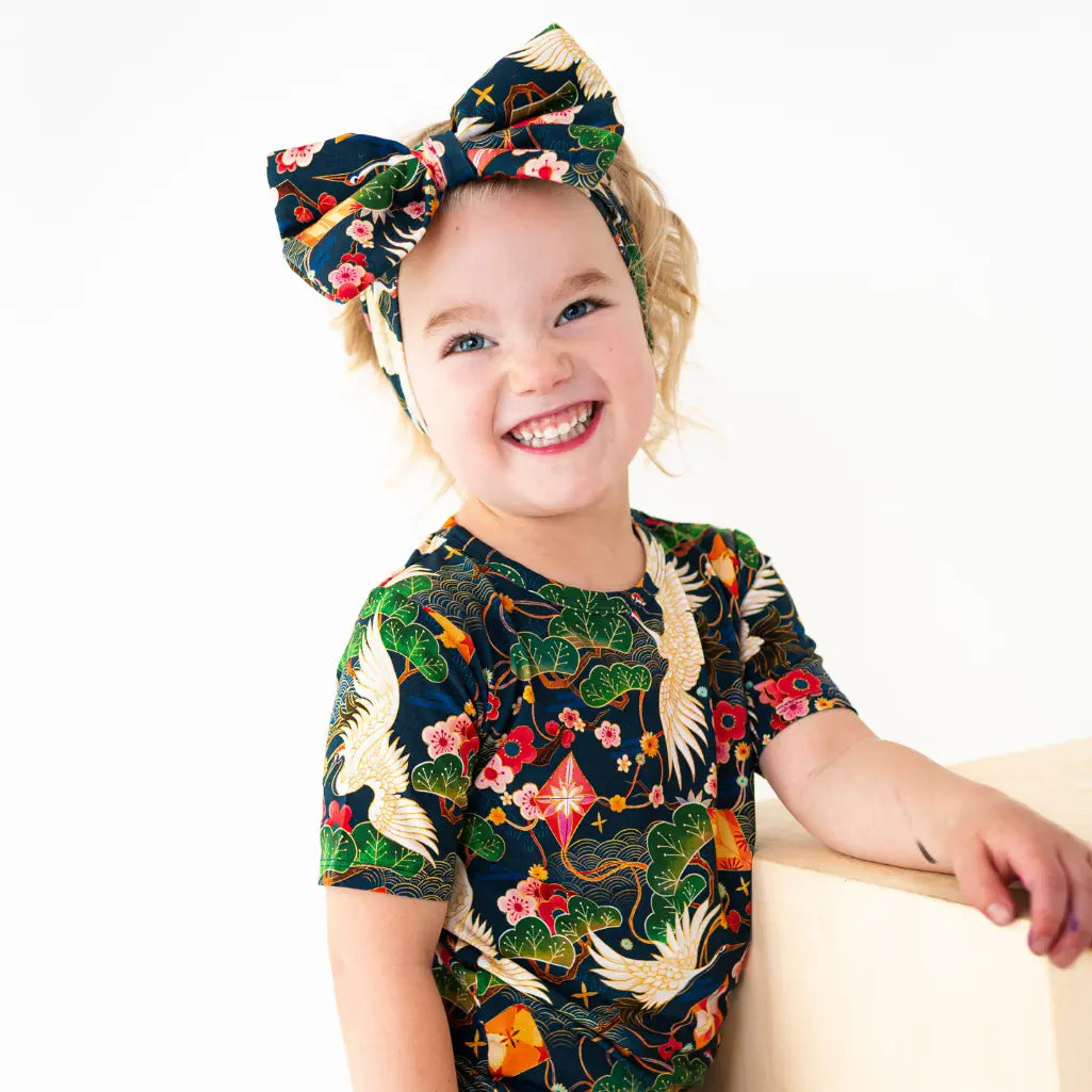 Child wearing a colorful outfit with floral and bird patterns on a white background