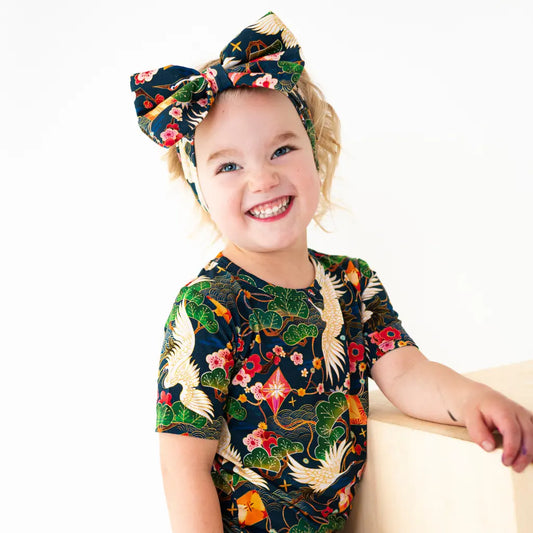 Child wearing a colorful outfit with floral and bird patterns on a white background