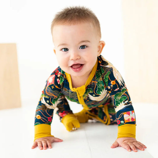 Baby crawling and smiling, wearing a dark floral print romper with yellow cuffs on a white background