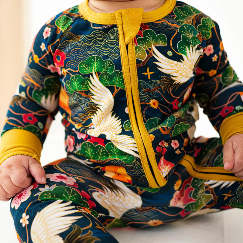 Child wearing a colorful outfit with floral and bird patterns, yellow zipper, and green accents.