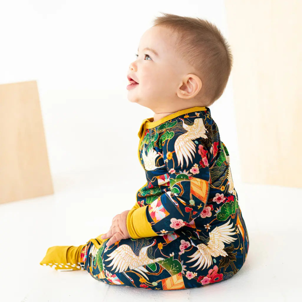 Baby wearing a colorful onesie with bird and floral patterns on a white background