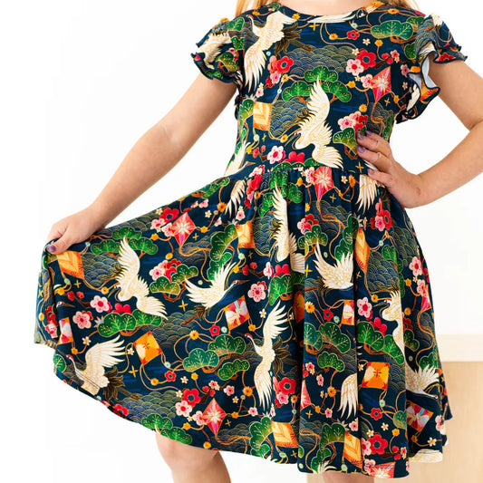 Child wearing a colorful dress with floral and crane patterns on a white background