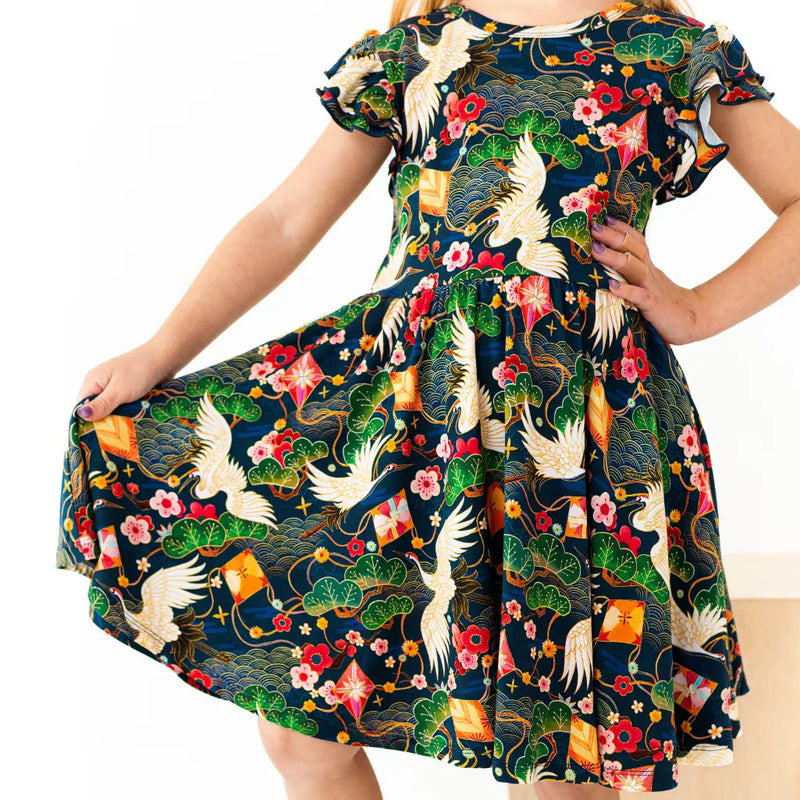 Child wearing a colorful dress with floral and crane patterns on a white background