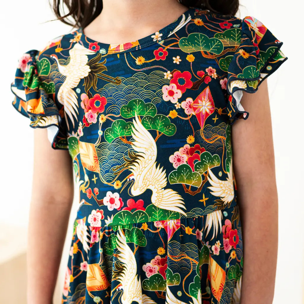 Child wearing a colorful dress with floral and bird patterns on a plain background