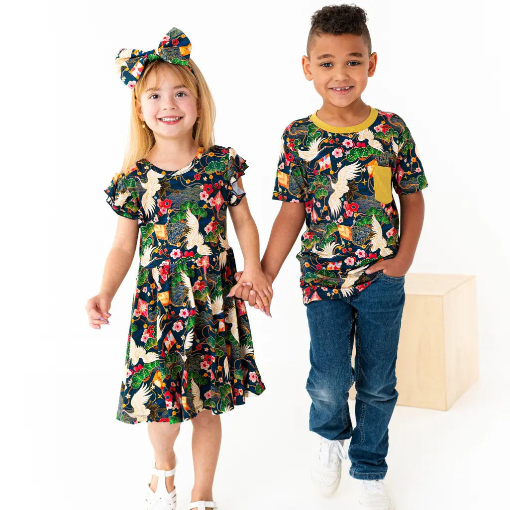 Two children holding hands, one in a floral dress and the other in a matching t-shirt and jeans, on a white background.