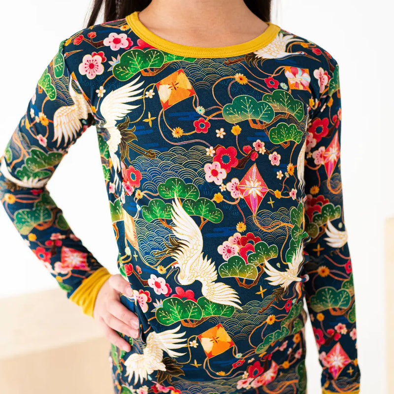 Person wearing a long-sleeve shirt with a colorful traditional pattern featuring cranes, flowers, and kites.