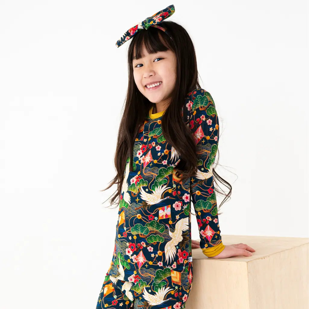 Child wearing a colorful patterned outfit with floral headband on a white background
