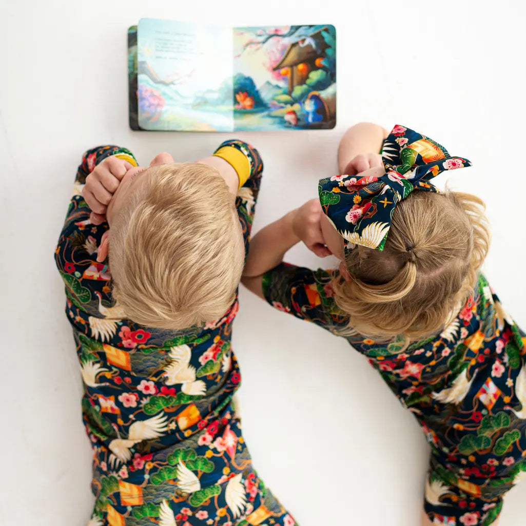 Two children in matching pajamas looking at a colorful book on a white surface.