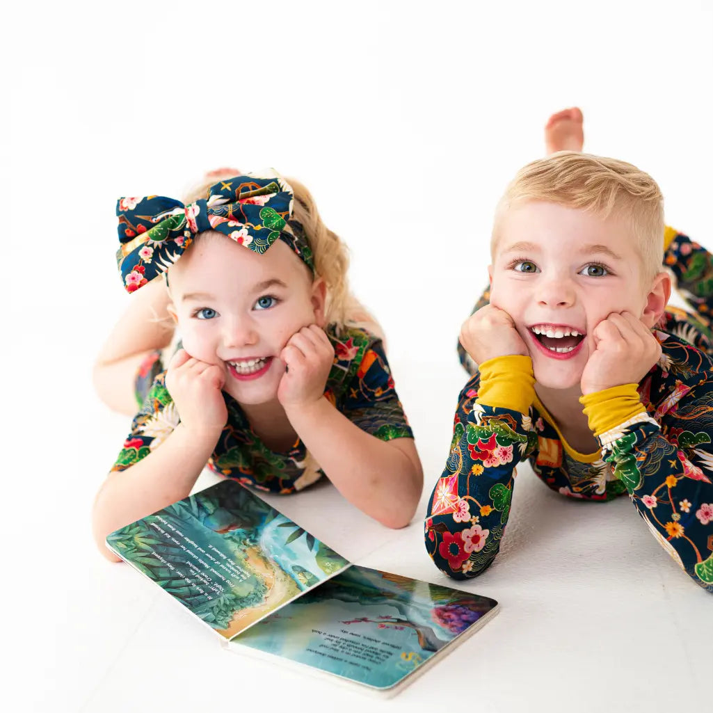 Two children in matching floral outfits with a book on a white background