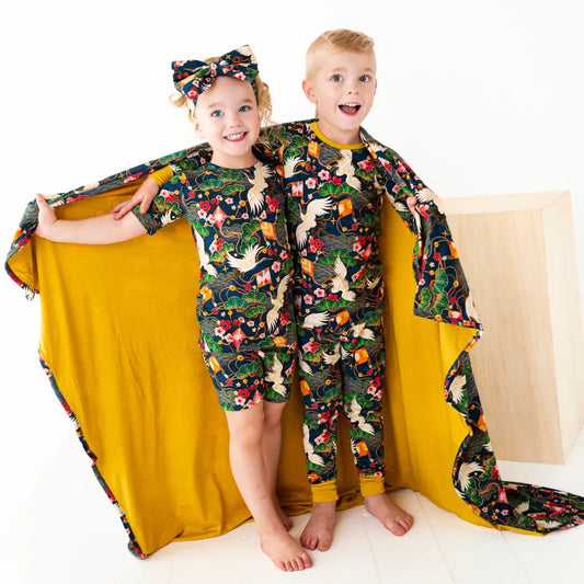 Two children wearing matching pajamas with a colorful design, standing behind a yellow blanket.