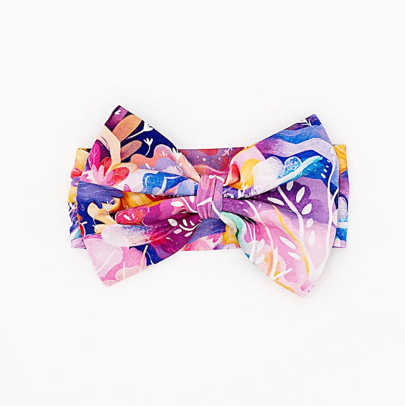 Colorful headband featuring a large bow with vibrant floral and abstract patterns on a white background
