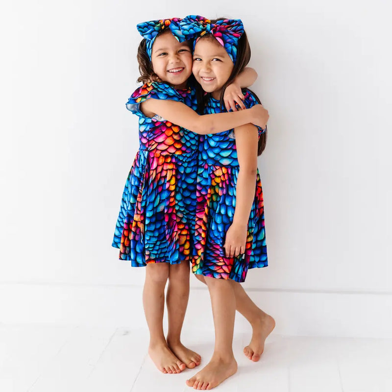 Two children wearing colorful dresses with a fish scale pattern on a white background