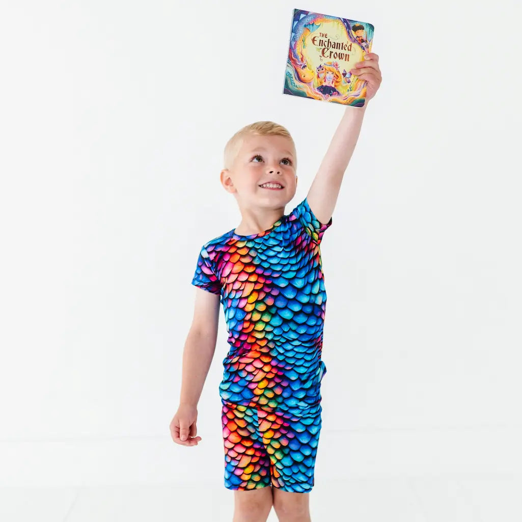 Child wearing a colorful dragon scale swimsuit holding a book.