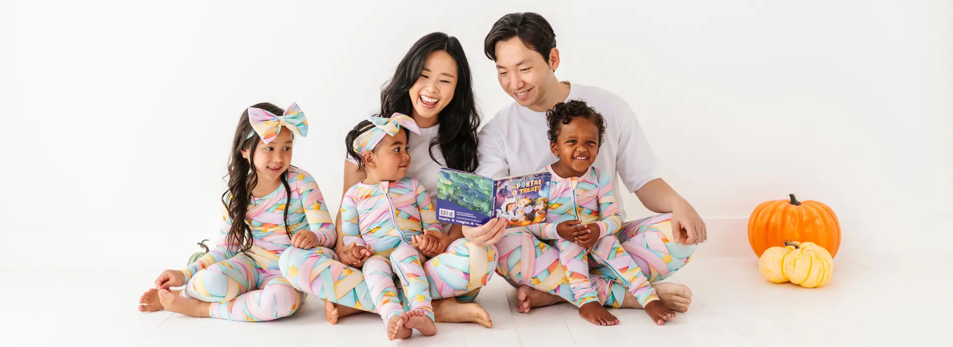 Family of four wearing matching pajamas with a white background and pumpkins.
