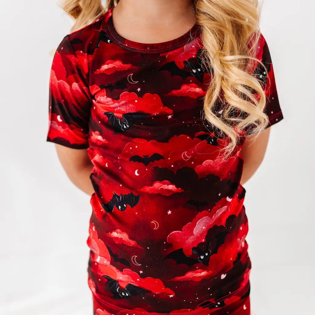 Child wearing a red and black bat-themed pajama set on a white background