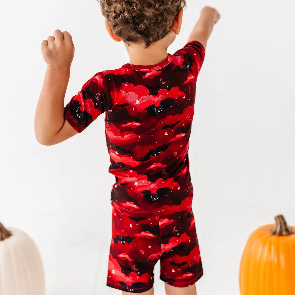 Child wearing a red and black bat-patterned outfit with pumpkins in the background