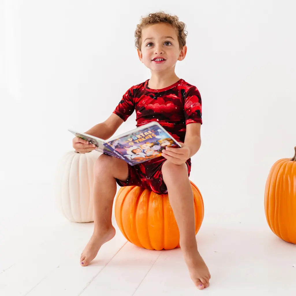 Child wearing a red and black bat-themed outfit on a white background