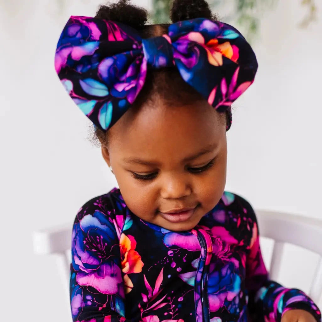 A baby wearing a headband with a whimsical floral pattern in hues of pink, purple, and blue.
