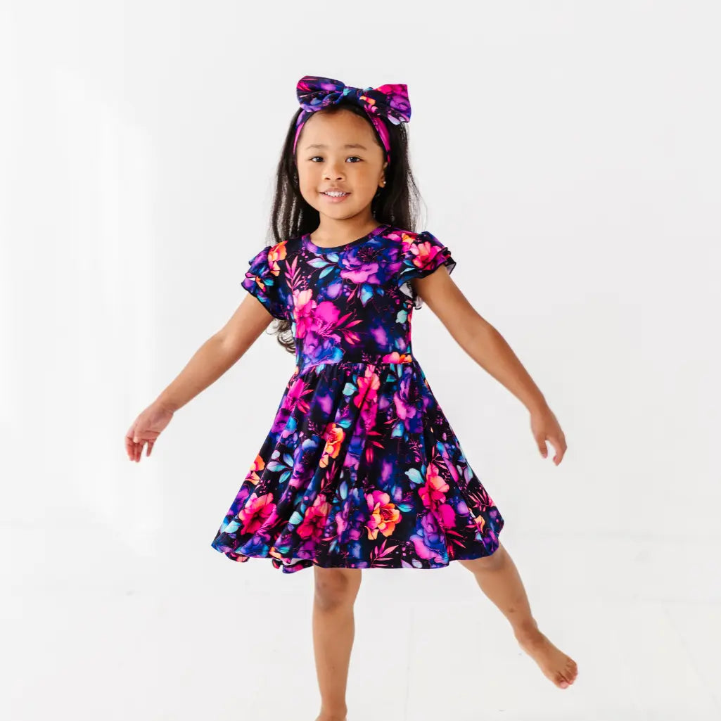 Young girl wearing a colorful floral dress and headband on a white background