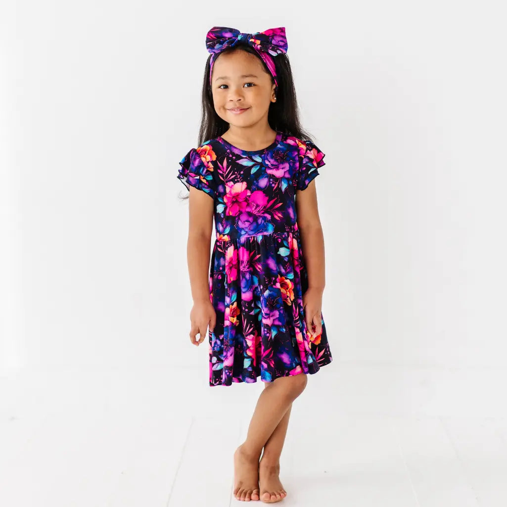 Young girl wearing a colorful floral dress and headband on a white background