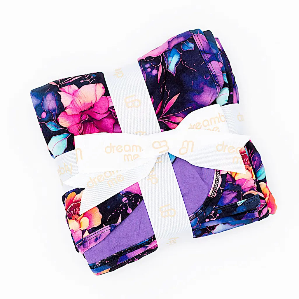 A brightly colored blanket with a floral pattern, wrapped with a white ribbon with gold text on it, against a white background.