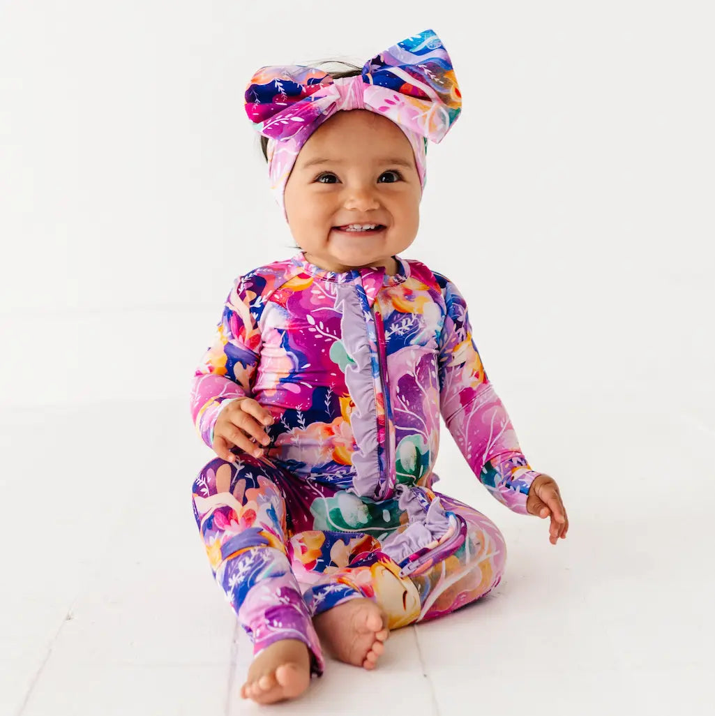 Baby in a colorful outfit with a large bow on a white background