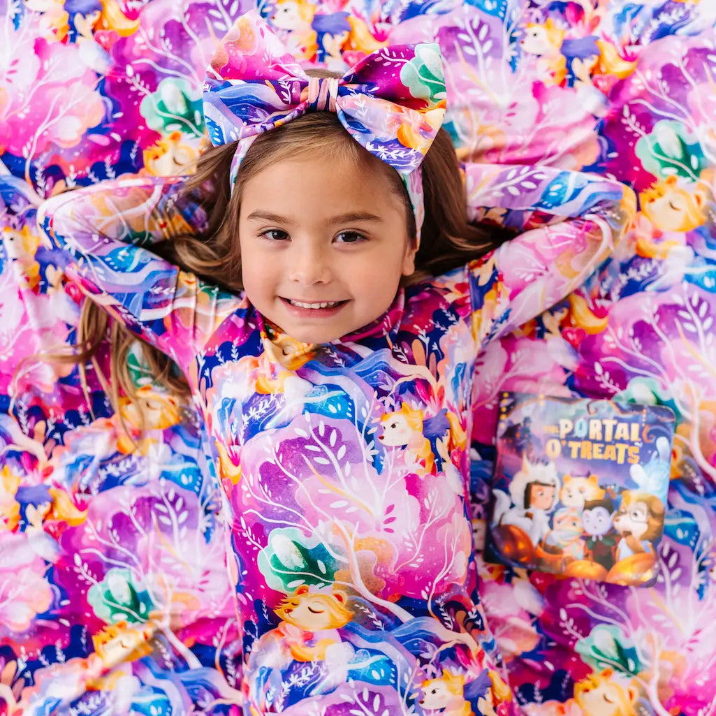 Child wearing a colorful outfit with a large bow, surrounded by similar patterned fabric.